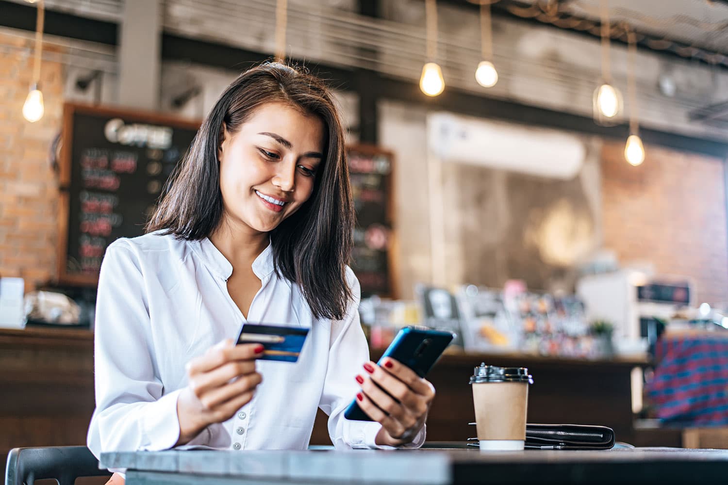 woman in coffee shop using credit card with her phone for mobile banking